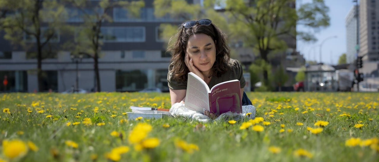 Femme couchée dans l'herbe et les pissenlits lit un livre.