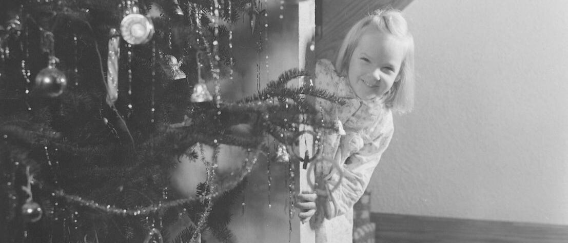 Une jeune fille se cache derrière un sapin de Noël.