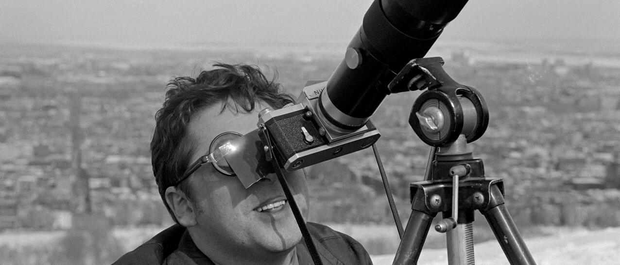 Homme portant lunettes fumées regardant dans l'objectif d'un appareil photo au long objectif.