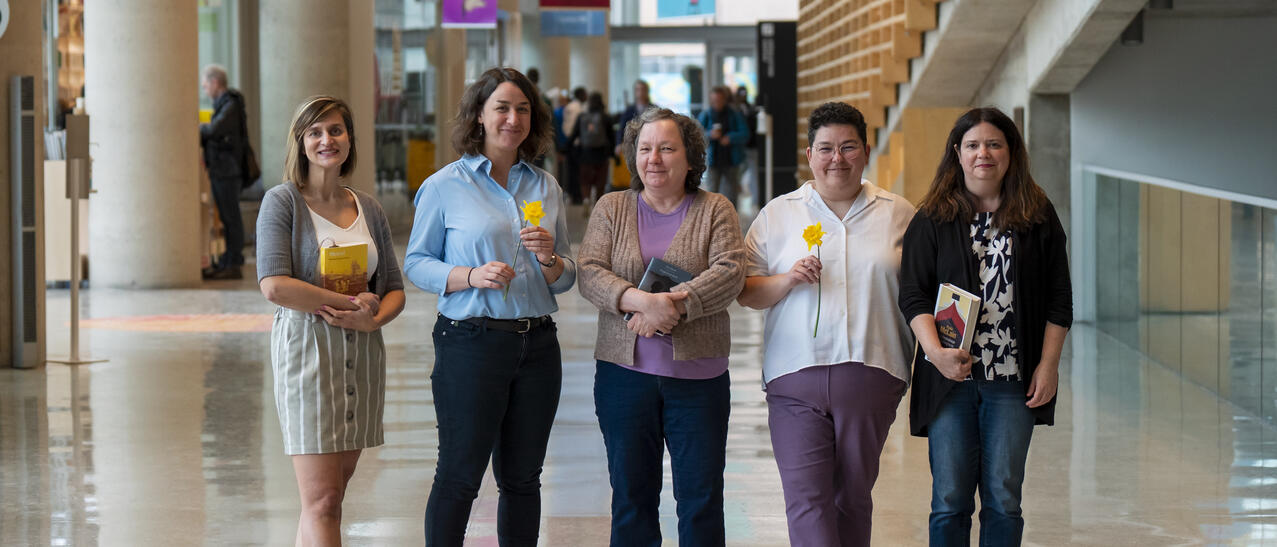 Cinq femmes, debout dans le hall de la Grande Bibliothèque, tiennent des livres dans leurs mains.