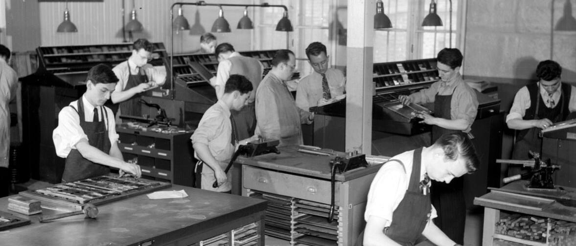 On aperçoit plusieurs jeunes hommes s'exerçant au métier de typographe. 