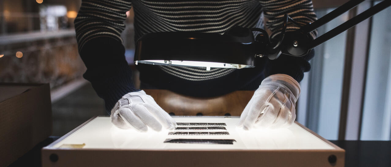 Un archiviste observe des négatifs sur une table lumineuse.