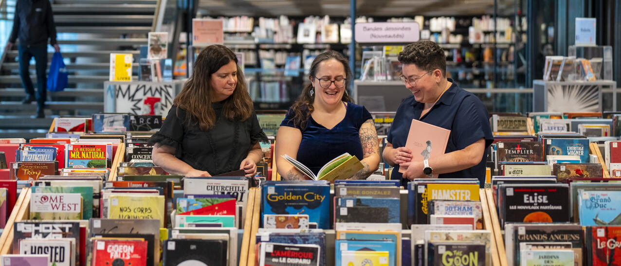 Trois femmes entourées de bacs remplis de bandes dessinées.