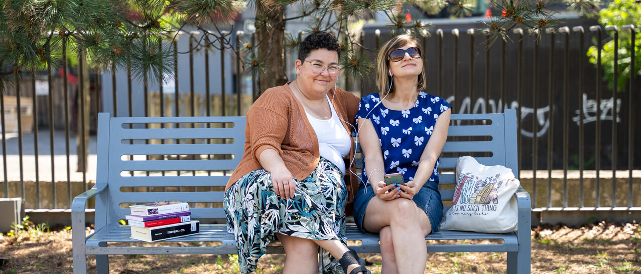 Deux femmes assises sur un banc de parc avec une pile de livres.