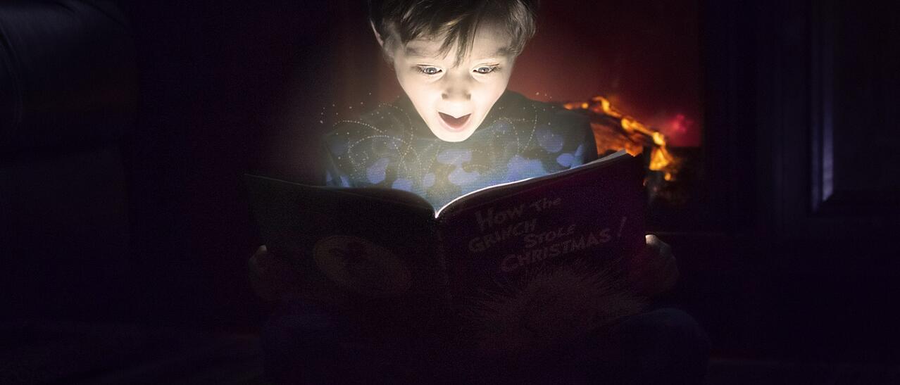 Un garçon est illuminé par le livre qu'il lit.