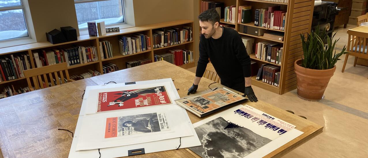 Un homme observe des affiches et des journaux sur une grande table en bois.
