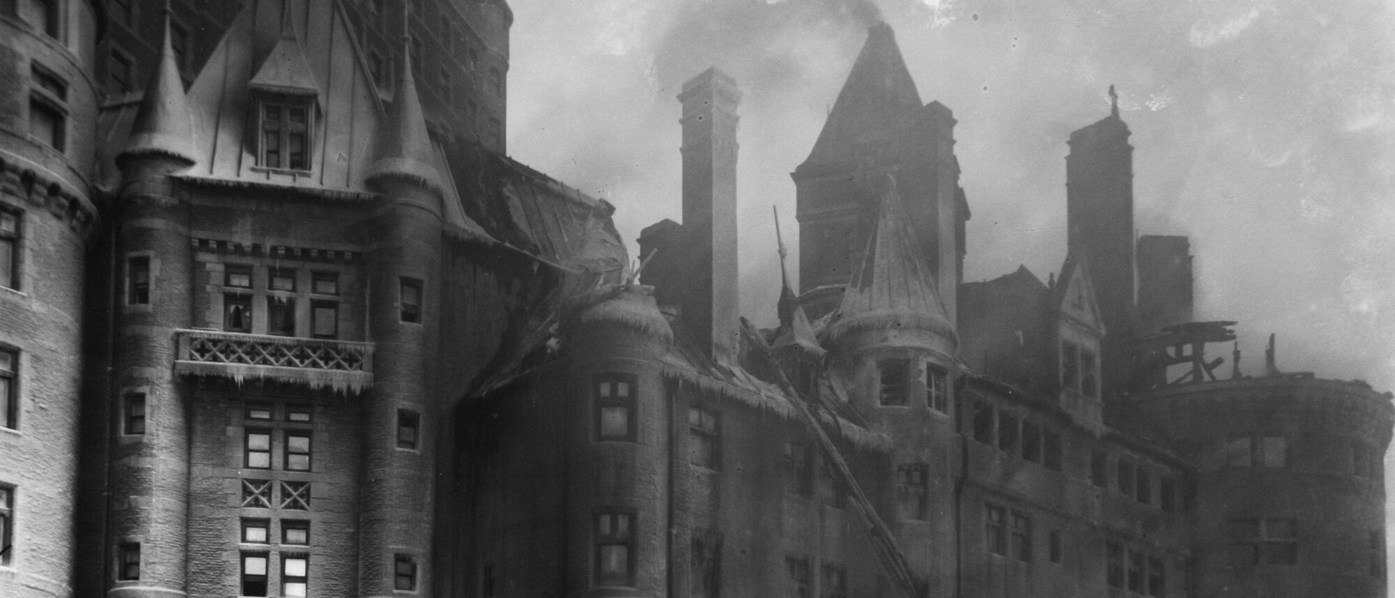 De la fumée s’échappe du Château Frontenac. Des pompiers se trouvent devant l’édifice, ainsi qu’une calèche et deux chevaux. 