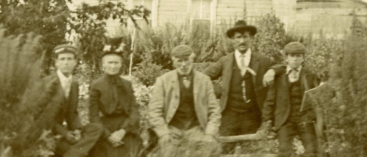 Cinq personnes assises à l’extérieur devant une maison en bois, entourées de végétation.