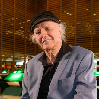 Gilles Vigneault souriant à la caméra dans les Chambres de bois de la Bibliothèque nationale au cœur de la Grande Bibliothèque