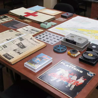 Des archives (diapositives, bandes magnétiques, négatifs, imprimés) exposés sur une table 