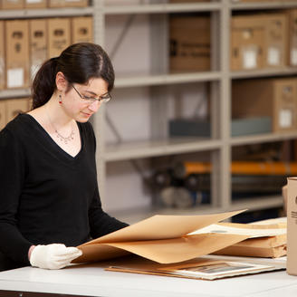 Employée des Archives nationales, entourée de boîtes d'archives, consultant des documents d'archives.
