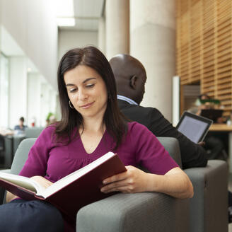 Une femme lisant un livre papier. Lui faisant dos, un homme lit sur une tablette numérique.