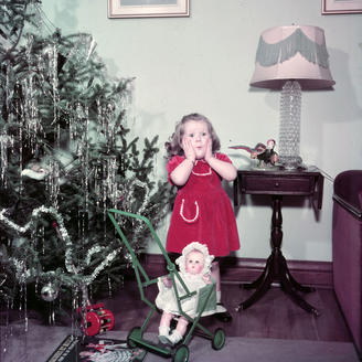 Fillette entourée de jouets, se tenant à côté d'un arbre de Noël.
