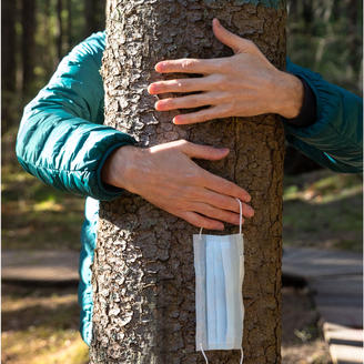 Une personne qui tient un masque de procédure dans sa main entoure un tronc d'arbre de ses deux bras.