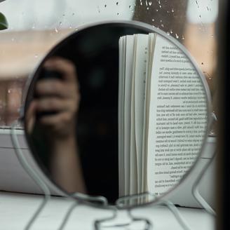 Reflet d'une main et d'un livre dans un miroir de table.
