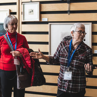 Deux femmes devant des tableaux accrochés à un mur.