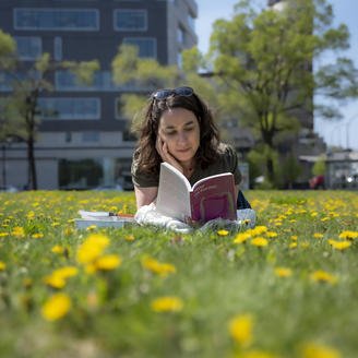 Femme couchée dans l'herbe et les pissenlits lit un livre.