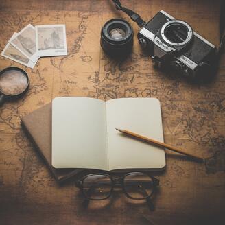 Objects sur une carte ancienne : loupe, appareil photo, carnet de notes, crayon, lunettes.