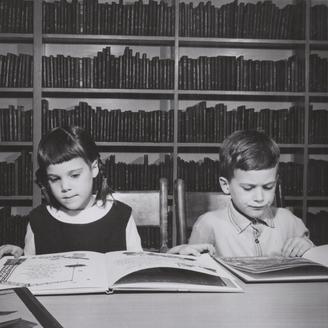 Un garçon et une fille lisent respectivement un livre, assis à une table à la bibliothèque.