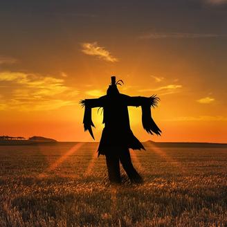 Un épouvantail au milieu d’un champ de blé; à l’horizon, le soleil se couche.