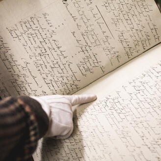 Une main pointe un texte dans un registre manuscrit