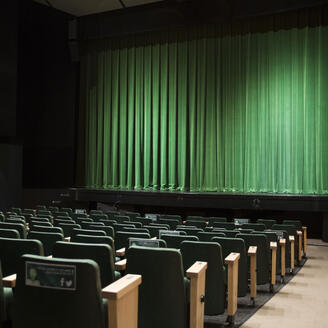 Salle de spectacle avec sièges et scène dotée d'un rideau vert.