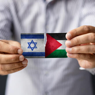 Un homme tient deux petits drapeaux partiellement déchirés. celui d'Israël et celui de la Palestine.