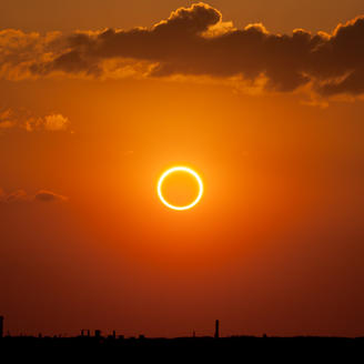 Photo d'un ciel rougeoyant. Au centre, l'anneau de feu créé par une éclipse de soleil.