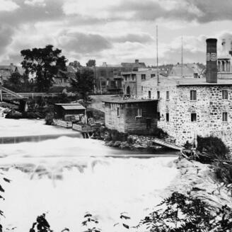 Photo noir et blanc montrant un édifice en briques pâles près d'une rivière.e
