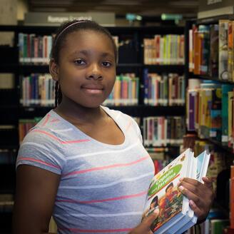 Photo couleur d'une jeune fille noire dans une bibliothèque.