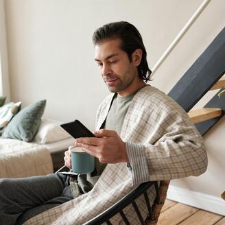 Photo d'un homme assis regardant son cellulaire et tenant un café