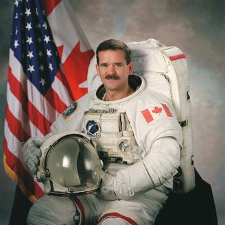 Chris Hadfield en costume de cosmonaute, son casque sur les genoux.