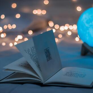 Un livre ouvert se trouve au premier plan alors qu'une boule bleue illuminée ressemblant à un globe et des guirlandes lumineuses figurent à l'arrière-plan 