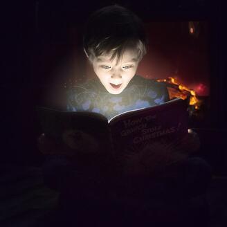 Un garçon est illuminé par le livre qu'il lit.
