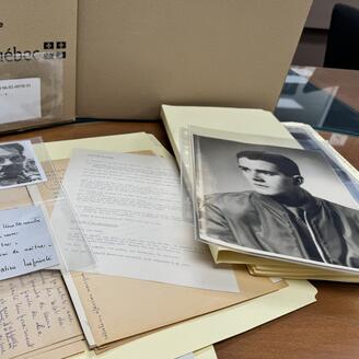 Archives sorties d'un carton sur un bureau avec des photos en noir et blanc, un mot manuscrit...