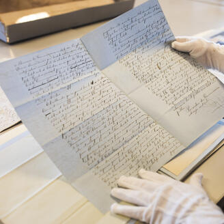 Une personne tient un document d'archives avec des gants blancs.