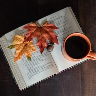 Livre ouvert sur lequel sont déposés des feuilles d'érable, une tasse de café et un gland