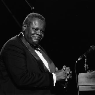 Oscar Peterson, assis au piano, sourit au public.