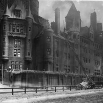 De la fumée s’échappe du Château Frontenac. Des pompiers se trouvent devant l’édifice, ainsi qu’une calèche et deux chevaux. 