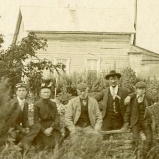 Cinq personnes assises à l’extérieur devant une maison en bois, entourées de végétation.
