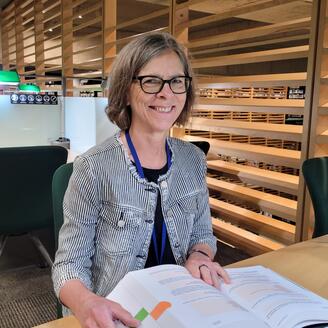 Photo de Claudine Legault, assise à une table et tenant un livre ouvert.