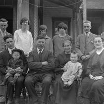 Photographie en noir et blanc d'une famille de 12 personnes placées sur deux rangées. Quatre personnes sont assises. Deux d'entre elles sont sur leur cuisses un bambin. Les six autres personnes sont debout derrière les chaises. 