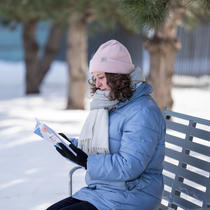 Une femme lit un livre sur un banc dans la neige.