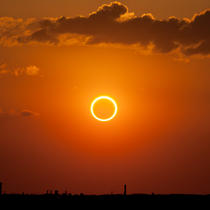 Photo d'un ciel rougeoyant. Au centre, l'anneau de feu créé par une éclipse de soleil.