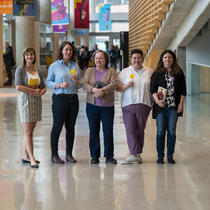 Cinq femmes, debout dans le hall de la Grande Bibliothèque, tiennent des livres dans leurs mains.