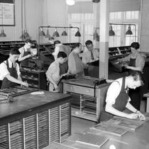 On aperçoit plusieurs jeunes hommes s'exerçant au métier de typographe. 