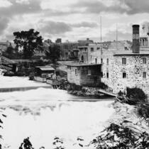 Photo noir et blanc montrant un édifice en briques pâles près d'une rivière.e