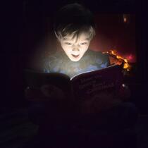 Un garçon est illuminé par le livre qu'il lit.