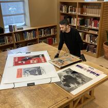 Un homme observe des affiches et des journaux sur une grande table en bois.