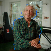 Le chanteur Richard Desjardins, souriant, entouré d'un piano et d'une guitare dans un chalet